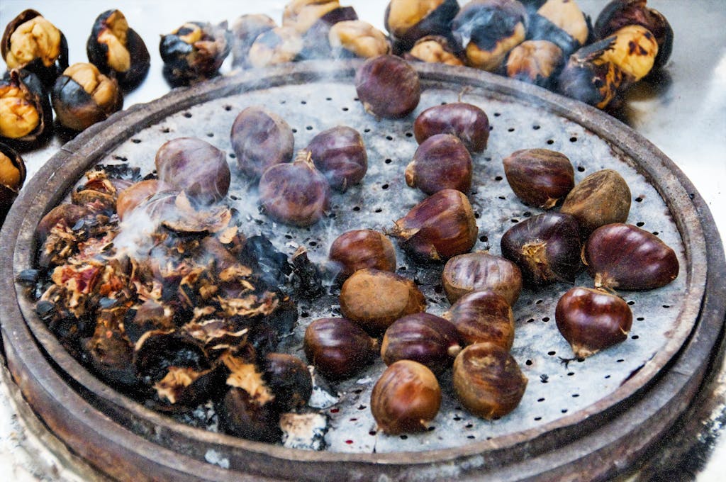 Close-up view of roasted chestnuts smoking on a round grill, emphasizing texture and warmth.